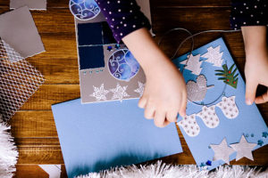 Little girl making Christmas cards on wooden background
